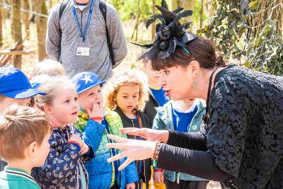 Photograph of person wearing a feathered fascinator speaking to children